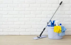 Cleaning supplies with mop bucket and gloves against a white brick wall