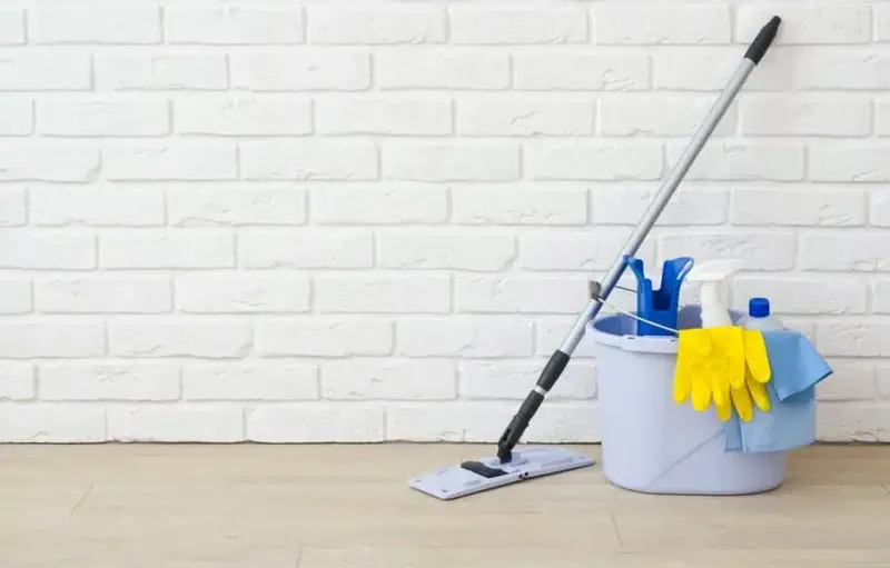 Cleaning supplies with mop bucket and gloves against a white brick wall