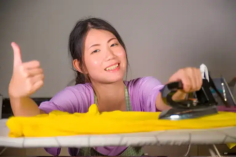 Woman ironing clothes in Singapore with steam iron on ironing board