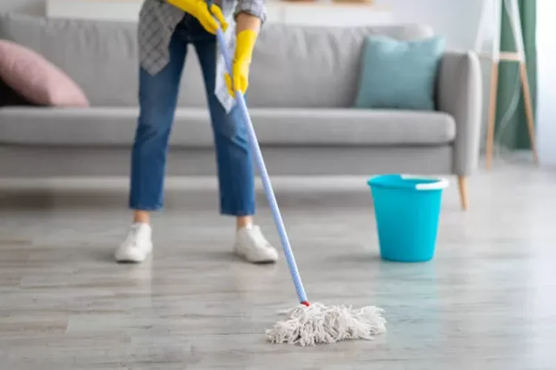 Person mopping a wooden floor in living room with blue bucket