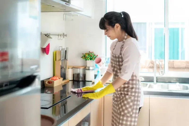 Asian woman cleaning kitchen counter with gloves and sponge