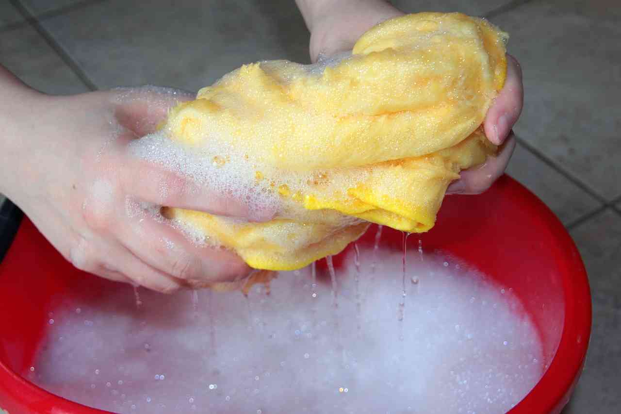 Hands squeezing a soapy yellow cloth over a red cleaning bucket.