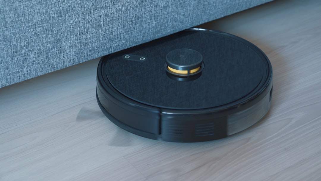Robot vacuum cleaner moving under a sofa on a wooden floor