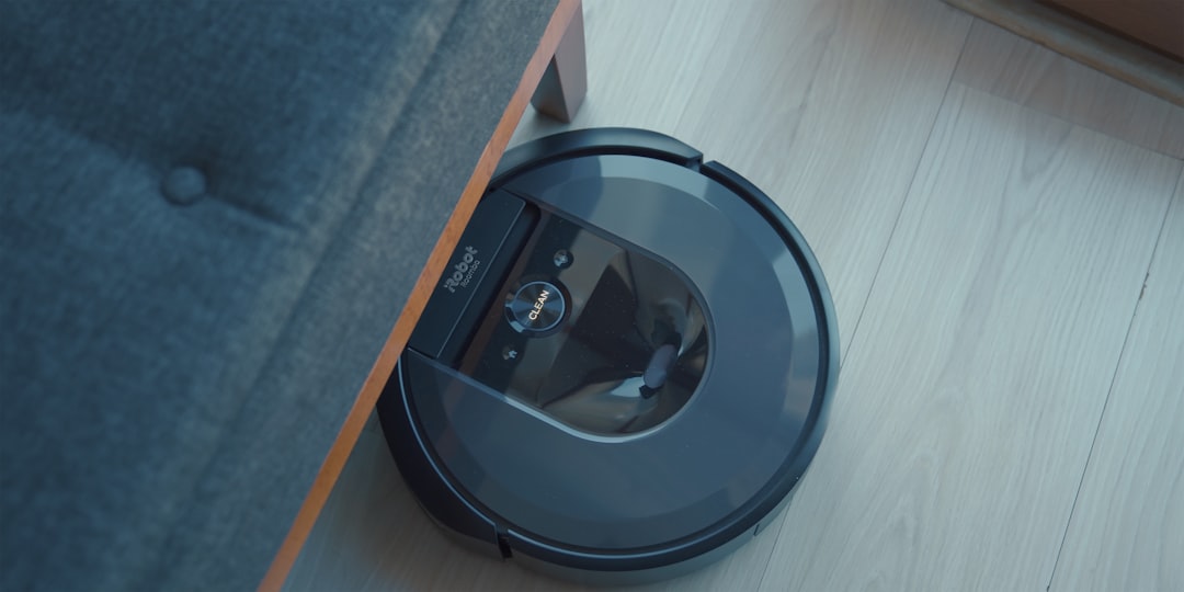 Robot vacuum cleaning under sofa on wooden floor.