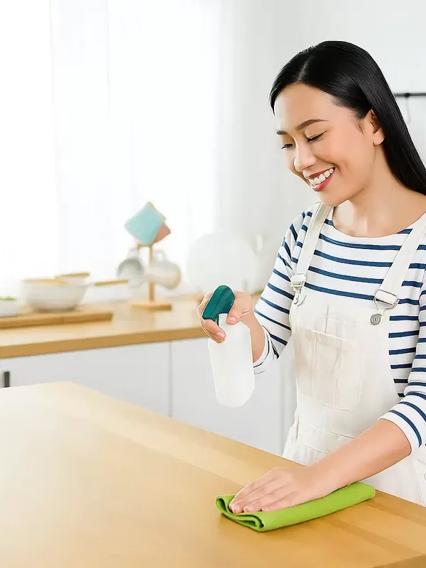 Smiling woman cleaning kitchen counter with spray bottle and cloth